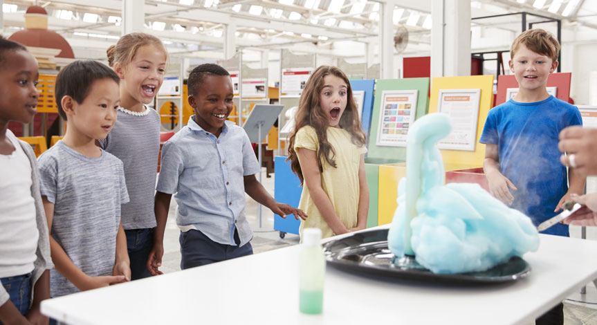 6 kids looking in amazement at an experiment where foam is coming out of a flask.