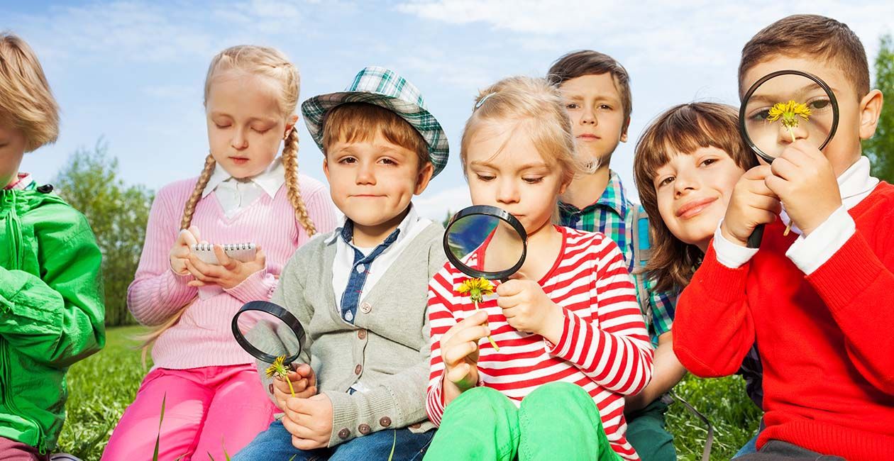 Kids sitting in a field while 3 of them are looking through a magnifying glass
