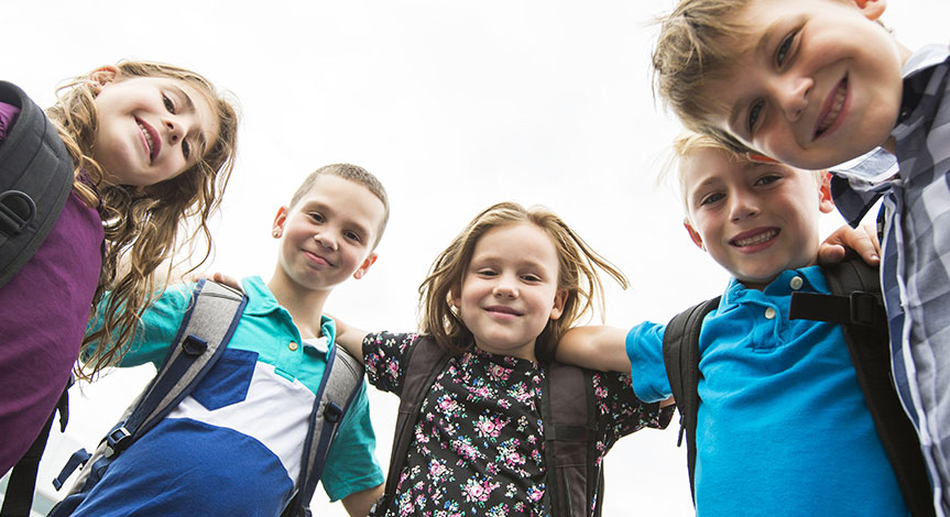 Kids looking down with arms around each all wearing school bags