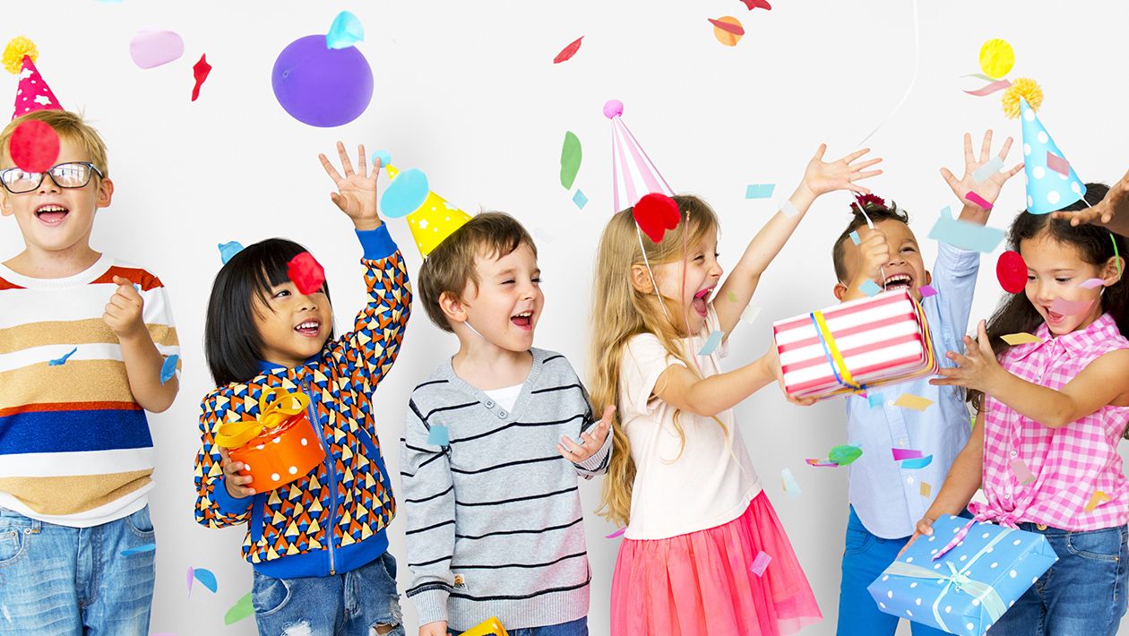 Group of kids celebrate birthday party together with presents, confetti and balloons