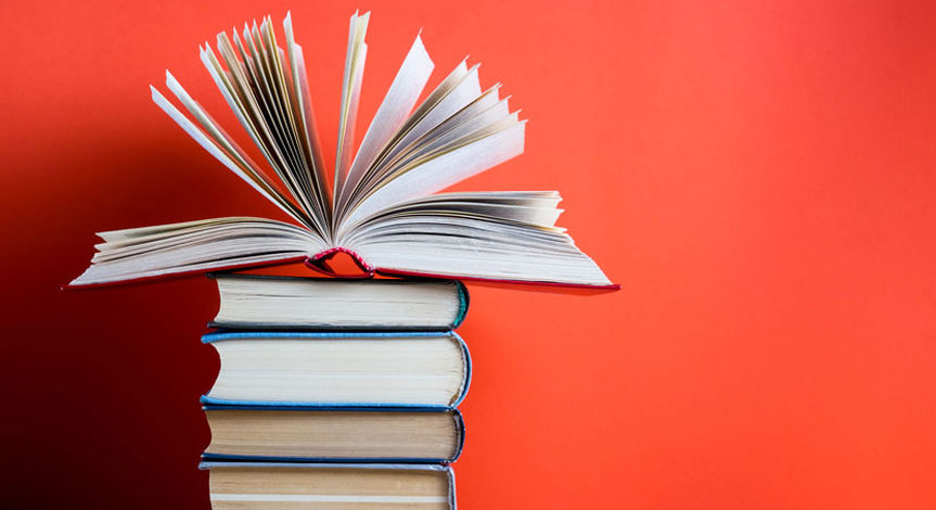 An open hard cover book on top of 4 other closed books with a red background.